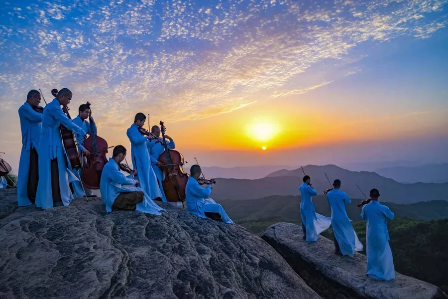 Monks playing the violin on a montain from the JInghui Guangxuan Symphony Orchestra.