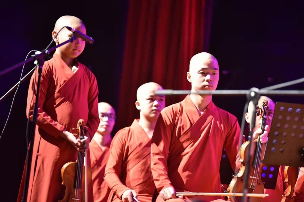 Monks singing in front of a mic, on a theater scene.